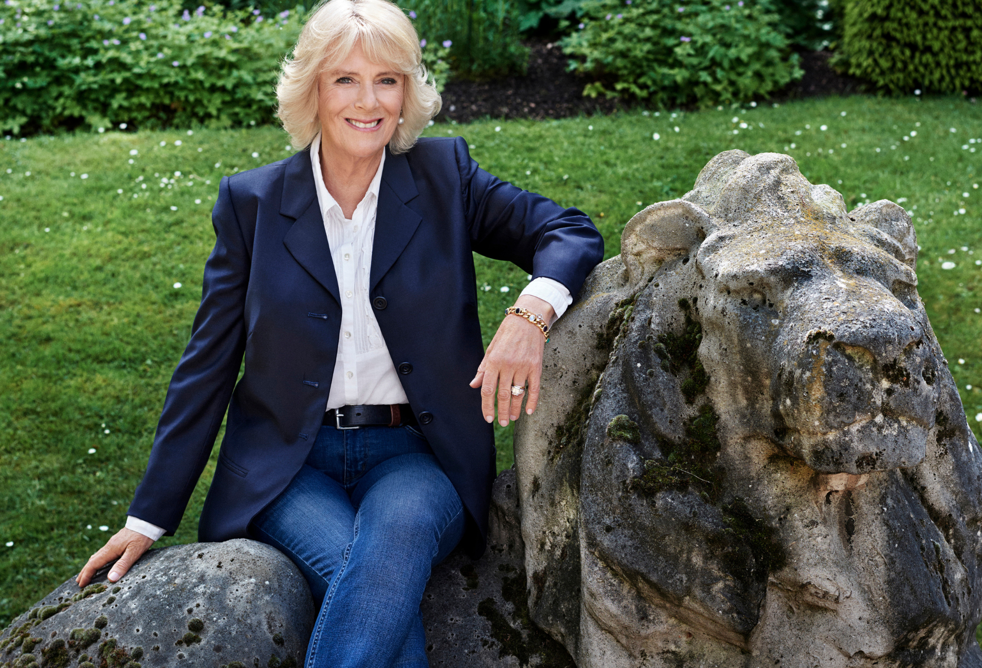 Queen Camilla sitting on a lion statue smiling at the camera
