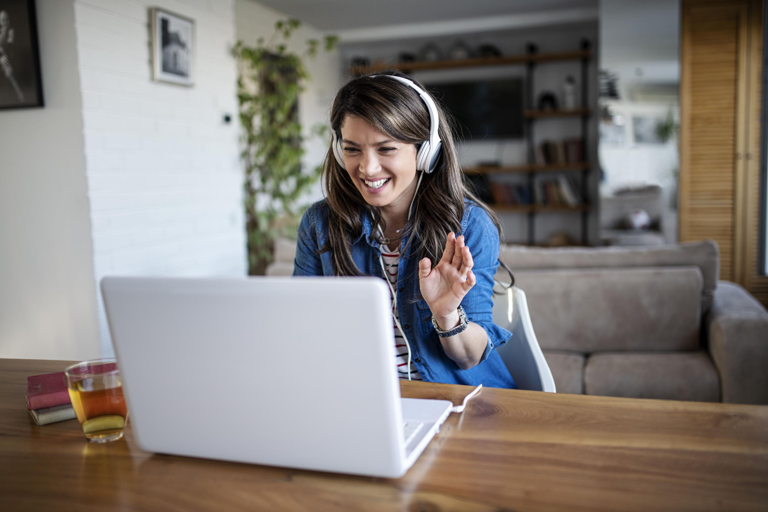younger woman wearing headphones, waving at laptop 