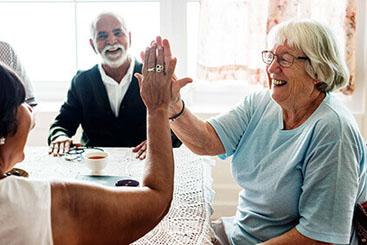A group of people sitting at a table smiling, two are high - fiving 