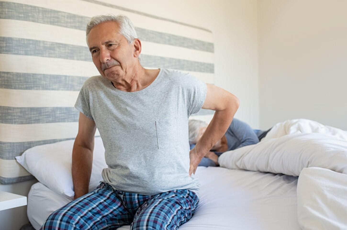 Man touching his sore back as he gets out of bed in the morning